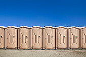 Portable toilets at the beach, in a row.