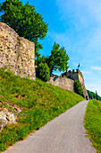 Frau zu Fuß auf einem Gehweg zu einem Schloss und Weinberg an einem sonnigen Sommertag in Morcote, Tessin, Schweiz.