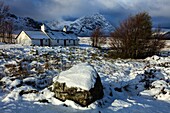 Black Rock Cottage on Rannoch Moor in the Scottish Highlands illuminated by the first rays of sunlight following an overnight snowfall in early November.