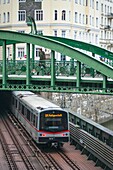 Der U-Bahn-Zug kommt aus einem Tunnel und fährt unter der Brücke Zollamtssteg hindurch, während er den Fluss in Wien, Österreich, überquert.
