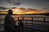 Silhouette of a man enjoying the sunset on the outside deck of a small riverboat, near Manaus, Amazon, Brazil, South America
