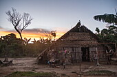 Die Sonne geht über strohgedeckten Hütten im Dorf Tijuca unter, nahe Manaus, Amazonas, Brasilien, Südamerika