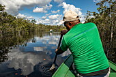 A Brazilian naturalist guide paddles a wooden pirogue canoe on the calm waters of a river, near Manaus, Amazon, Brazil, South America