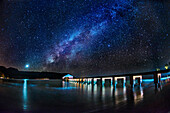 Die Milchstraße und die Venus erheben sich über der Hanalei Bay mit dem Hanalei Pier im Vordergrund, der von vorbeifahrenden Autoscheinwerfern beleuchtet wird, Hanalei, Hawaii, Vereinigte Staaten von Amerika, Pazifik