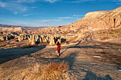 Turkey, Cappadocia, Rear view of woman in red dress walking in rocky landscape