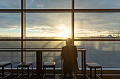 Großbritannien, London, Rückansicht der Frau am Flughafenterminal bei Sonnenuntergang