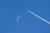 Airplane leaving contrails against blue sky with waning moon