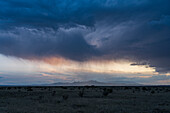 USA, New Mexico, Santa Fe, Storm clouds and rain above desert landscape