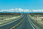 USA, Nevada, Winnemucca, Highway 95 crossing desert landscape with snowcapped mountains in distance