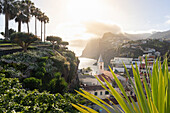 Sonnenuntergang über den weißen Gebäuden von Camara de Lobos, eingerahmt von Pflanzen, Insel Madeira, Portugal, Atlantik, Europa