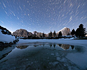 Polar star trail in the night sky over Lagazuoi and Tofana di Rozes peaks from frozen lake Limides, Dolomites, Veneto, Italy, Europe