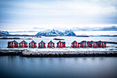 Luftaufnahme von roten Rorbu-Hütten in einer Reihe inmitten des kalten Meeres im Winter, Svolvaer, Nordland County, Lofoten-Inseln, Norwegen, Skandinavien, Europa