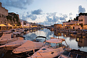 Blick vom Kai über den Hafen in der Abenddämmerung, Lichter spiegeln sich in ruhigem Wasser, Ciutadella (Ciudadela), Menorca, Balearen, Spanien, Mittelmeer, Europa