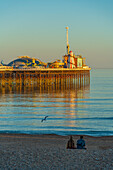 Ansicht des Paares am Strand und Brighton Palace Pier bei Sonnenuntergang, Brighton, East Sussex, England, Vereinigtes Königreich, Europa