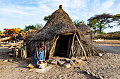 Frau mahlt Sorghum vor einer traditionellen Hütte des Stammes Toposa, Eastern Equatoria, Südsudan, Afrika
