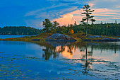 Kanada, Ontario, Distrikt Kenora. Herbstfarben des Waldes spiegeln sich bei Sonnenuntergang auf dem Middle Lake wider