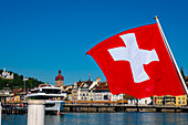 Schweizer Flagge in der Stadt Luzern mit See an einem sonnigen Sommertag in Luzern, Vierwaldstättersee, Schweiz.