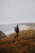 Man hiking on hill overlooking tranquil ocean beach, Sandwood Bay, Assynt, Scotland