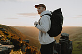 Male hiker with backpack on top of mountain at sunset, The Trinnacle, Derbyshire, England
