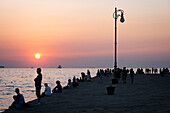 Blick auf die Menschen auf der Mole bei Sonnenuntergang im Hafen von Triest, Friaul-Julisch-Venetien, Oberitalien, Italien, Europa