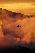 Rauchiger Sonnenuntergang und Hubschrauber bei der Brandbekämpfung in Burnside, Dunedin, Südinsel, Neuseeland