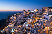 Griechenland, Santorin. Das Dorf Oia erstrahlt im Licht des Sonnenuntergangs, wenn die Lichter der Stadt dieser ikonischen Szene ihren Zauber verleihen.