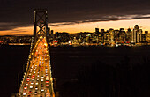San Francisco Kalifornien Skyline und die Oakland Bay Bridge am Abend mit Verkehr auf der Brücke und Autos am bunten Himmel Sonnenuntergang von Treasuire Island