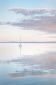 Sailboat and morning clouds reflected in calm waters of Bellingham Bay, Washington State