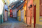 Siebenbürgen, Rumänien, Kreis Mures, Sighisoara, Wohnstraße mit Kopfsteinpflaster und bunten Häusern im Dorf. UNESCO-Weltkulturerbe.