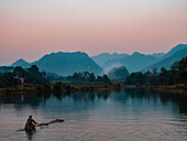 Asien, Vietnam, Naturschutzgebiet Pu Luong. Ein einsamer Mann nimmt ein einfaches Floß auf den Fluss für eine Bootsfahrt bei Sonnenuntergang.