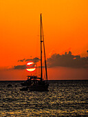 Seven Mile Beach, Grand Cayman. Segelboot und ein Boot mit orangefarbenem Sonnenuntergang hinter den Wolken am Karibischen Meer