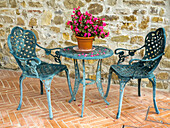 Europa, Italien, Chianti. Tisch und Stühle mit einer blühenden Begonie in der Mitte vor einer Steinmauer in einem Weinberg.