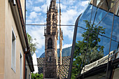 Bell tower of the Cathedral reflected in a glass building, under clouded sky Bolzano, South Tyrol, Italy