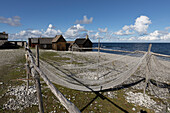Fischernetz an einem Kieselstrand. Im Hintergrund Holz Fischerhütten. Farö, Gotland, Schweden.