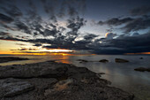 Sonnenuntergang am Meer. Felsig. Regenwolke im Hintergrund. Abendrot. Himmel spiegelt im Wasser. Lauterhorn, Gotland, Schweden.