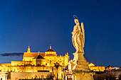 Statue des Erzengel Raphael auf der römischen Brücke und die Mezquita in der Abenddämmerung, Cordoba, Andalusien, Spanien  