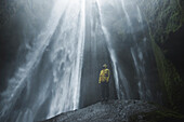 Man wearing yellow raincoat by Seljalandsfoss waterfall in Iceland