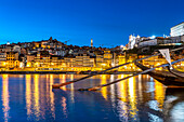 Blick über die traditionellen Rabelo Boote am Douro Ufer in Vila Nova de Gaia auf die Altstadt von Porto in der Abenddämmerung, Vila Nova de Gaia, Portugal, Europa