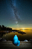 Frau sitzt auf dem Steg am See und betrachtet den Sternenhimmel im Tiveden National Park, Schweden, Skandinavien, Europa