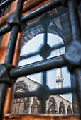 Istanbul city, a landmark, a tall minaret and arches with stonework and fretwork detail, and view through metal gates o bars.