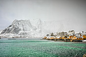 Insel Sakrisoya, die Bergküste und Kleinstadt im Archipel der Lofoten, Winter, Graupel, Schnee und Nebel.
