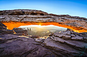 Sunrise at Mesa Arch in Canyonlands National Park at sunrise, the sun lighting the glowing sandstone underside of the arch.