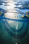 The Sydney Harbour Bridge, the shadow of the arch on the water, and aerial view of the landscape.