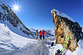 Three people on ski tour stand under rock tower and look at Zillertal Alps, Höllensteinkar, Tux Valley, Zillertal Alps, Tyrol, Austria