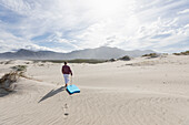 Teenager-Mädchen (16-17) geht mit Bodyboard auf Sanddünen im Naturschutzgebiet Walker Bay, Hermanus, Südafrika