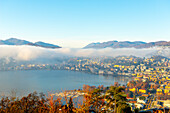 Bergkette über Wolkengebilde und Luganersee mit Sonnenlicht und klarem Himmel in der Stadt Lugano, Tessin in der Schweiz.