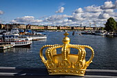 Golden crown on Skeppsholmen bridge with boats in harbor behind, Stockholm, Sweden, Europe