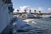 Wellen brechen gegen "Klein-Venedig" mit den berühmten Windmühlen von Mykonos im Hintergrund, Mykonos, Südliche Ägäis, Griechenland, Europa