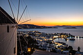Windmill in front of the 180º Sunset Bar overlooking the town with the famous Mykonos windmills, harbor and islands at dusk, Mykonos, South Aegean, Greece, Europe