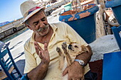 Älterer griechischer Mann gibt seinem Hündchen ein High Five im Restaurant Lombranos Taverna, Fira, Santorini, Südliche Ägäis, Griechenland, Europa